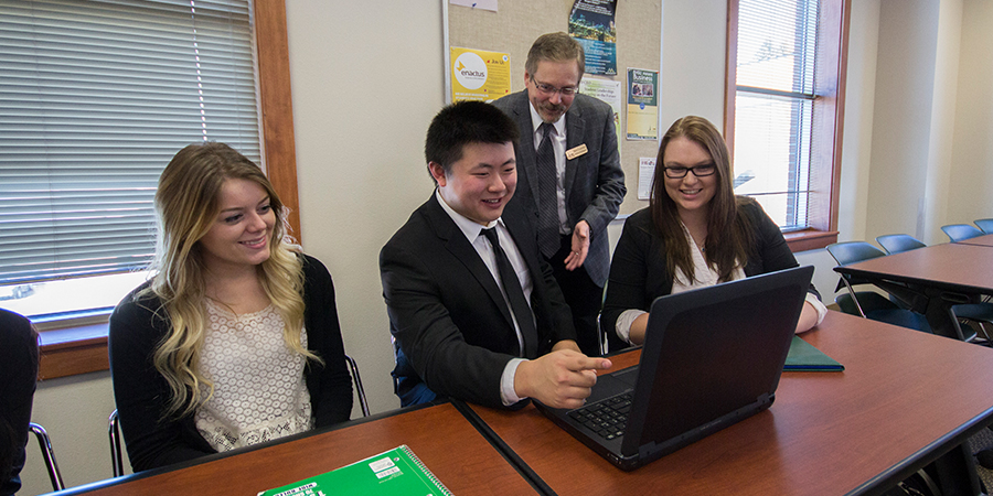 Three students and an advisor look at a computer screen.