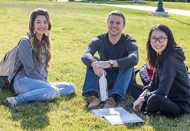 Three students pose for a photo on the campus green.