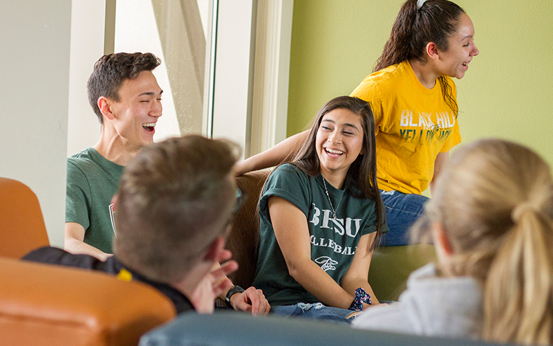 Five students laughing in a residence hall lobby.