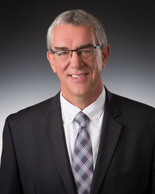 Headshot of Bob Mundt, a smiling man with short hair and glasses wearing a suit and tie, facing the camera.