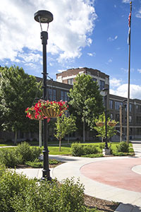 Picture of BHSU Woodburn Hall, lots of green plants and red flowers, with sidewalk