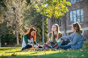 Three female BHSU students sitting on the campus green and talking