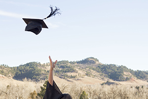 BHSU graduate throwing graduation cap up into the air, hills in the background