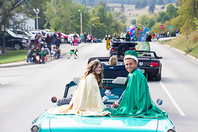 The BHSU Homecoming Queen (left) and Homecoming King (right) sit on the back of a car for a parade.