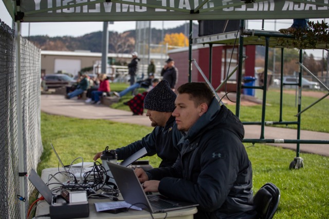 Two men at a sporting event table with computers