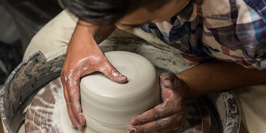 Student throws clay on a pottery wheel