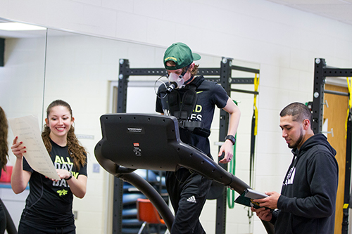 One student runs on a treadmill while two students monitor.