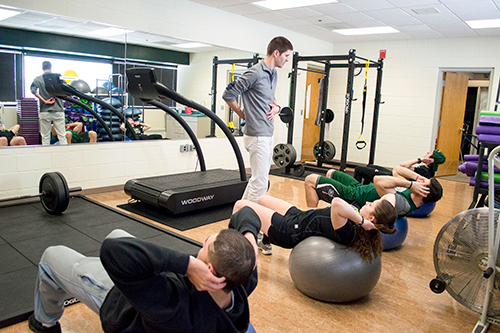 Four students do sit-ups while an advisor stands.