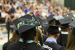 Students sitting at graduation, showing their graduation caps to the camera.