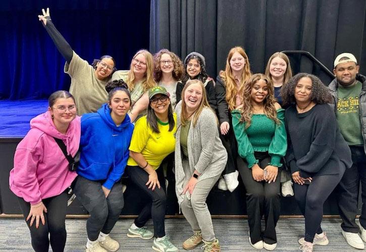 Twelve international students pose with Kaitlin Palmer, Director of International Relations, at a conference or convention.