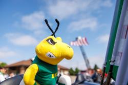 A close-up of a BHSU Yellow Jacket mascot (Sting) stuffed animal mounted on a motorcycle, with a bright blue sky and a flag in the background.