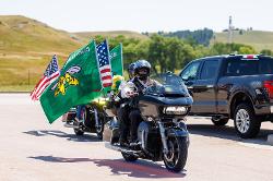 A motorcyclist rides with BHSU Yellow Jacket flags and American flags displayed on the back of their bike during the annual Jacket Ride.