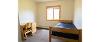 Single bedroom of a Yellowjacket Apartment, showing the desk along the left side of the room, and the bed along the right side. 