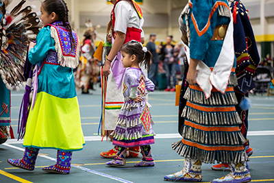 A young indigenous girl and three others prepare to dance at a powwow.