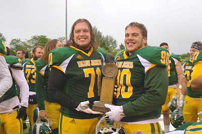 Two BHSU football players hold the Homestake Trophy.