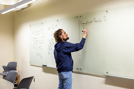 Man in a classroom writes on a whiteboard.