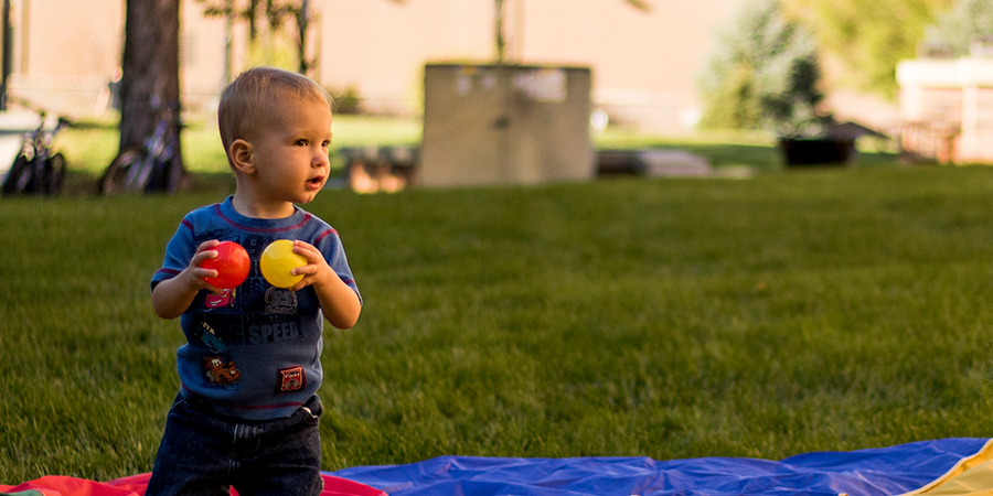 A very young boy holds two plastic balls.
