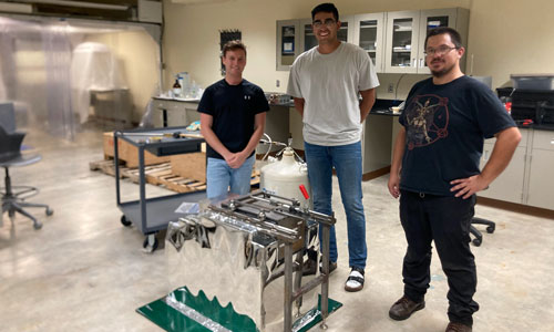Picture of three men standing together next to a High Purity Germanium (HPGe) detector, SOLO, in the BHSU above ground lab