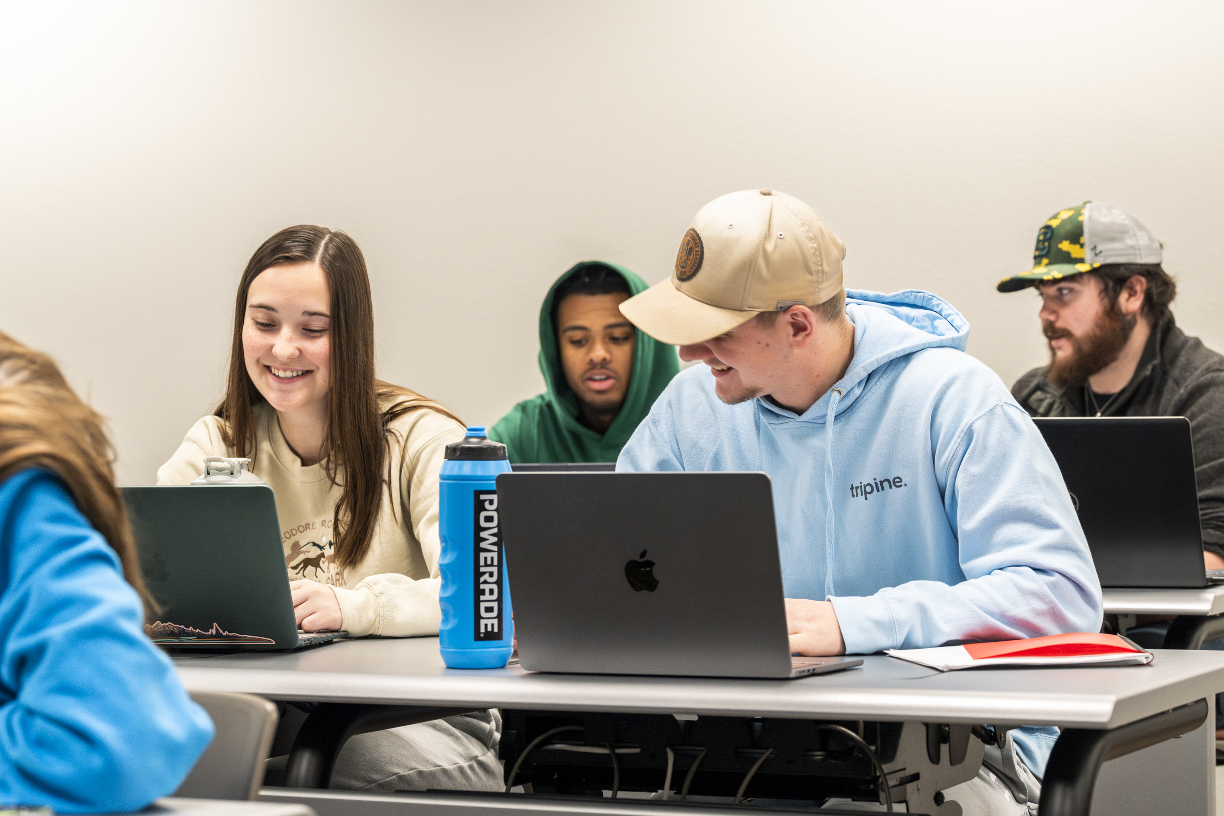 Four students sit in a classroom looking at their laptops.