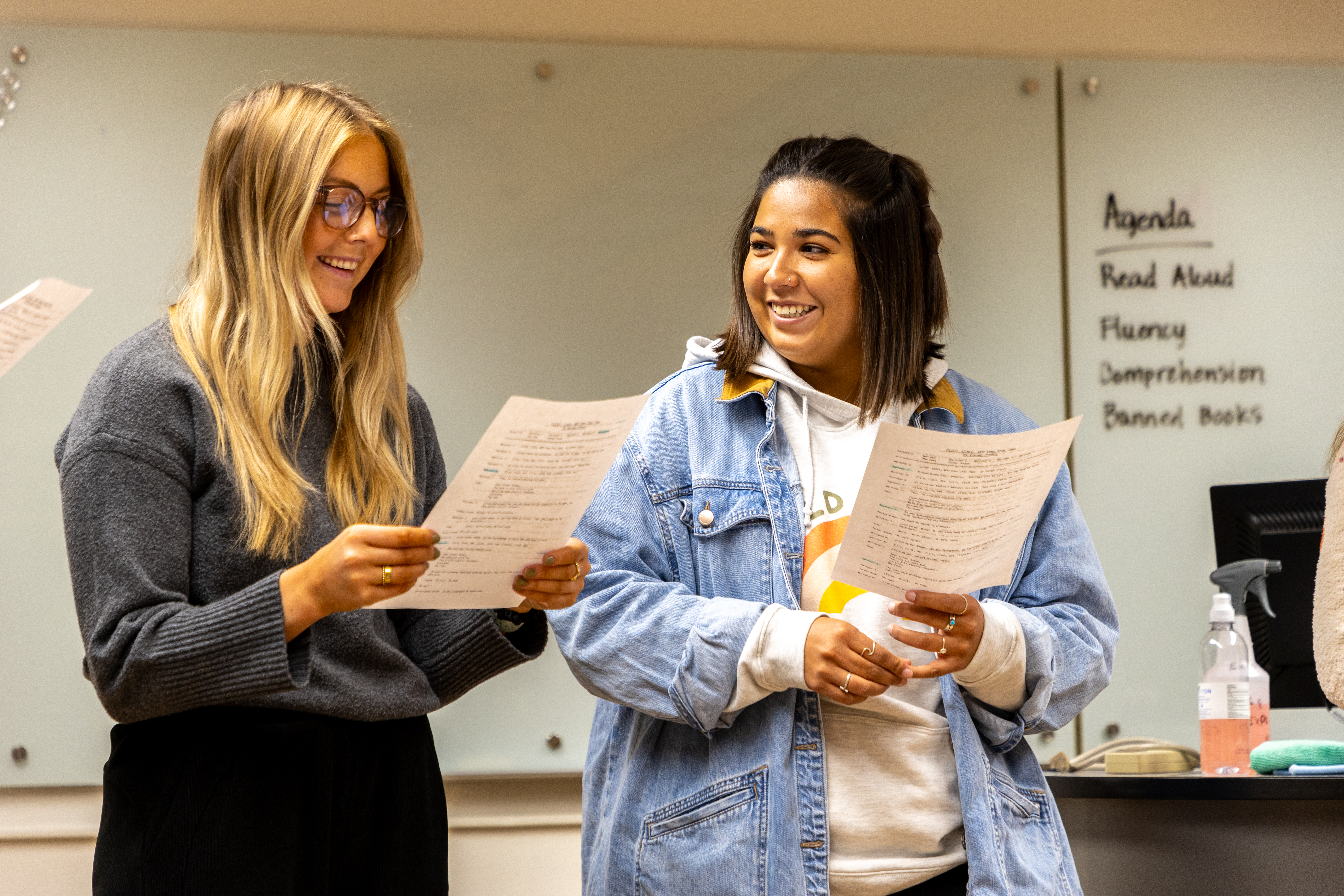 Two education students stand together, each reading off of a paper that they are holding.