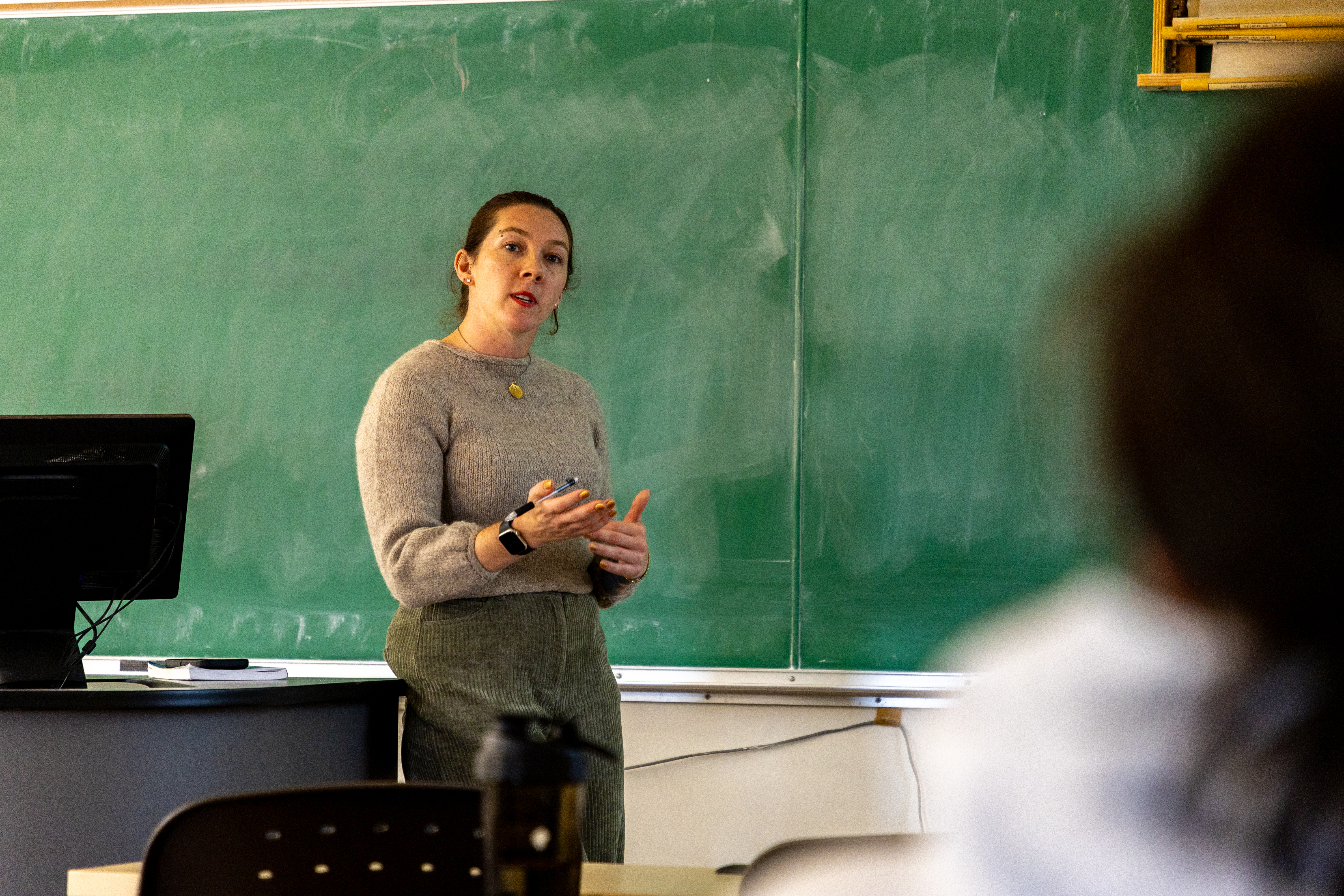 A professor lectures in front of a chalk board.