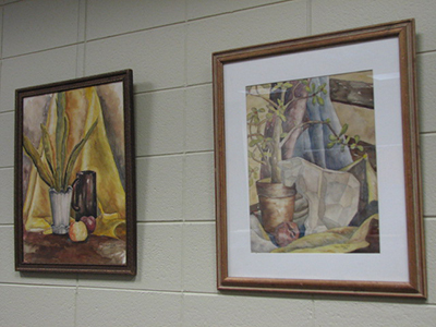 Two of Mar Gretta Cocking's watercolor paintings on a grey wall.