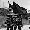 Four men marching, holding either a flag or a gun.