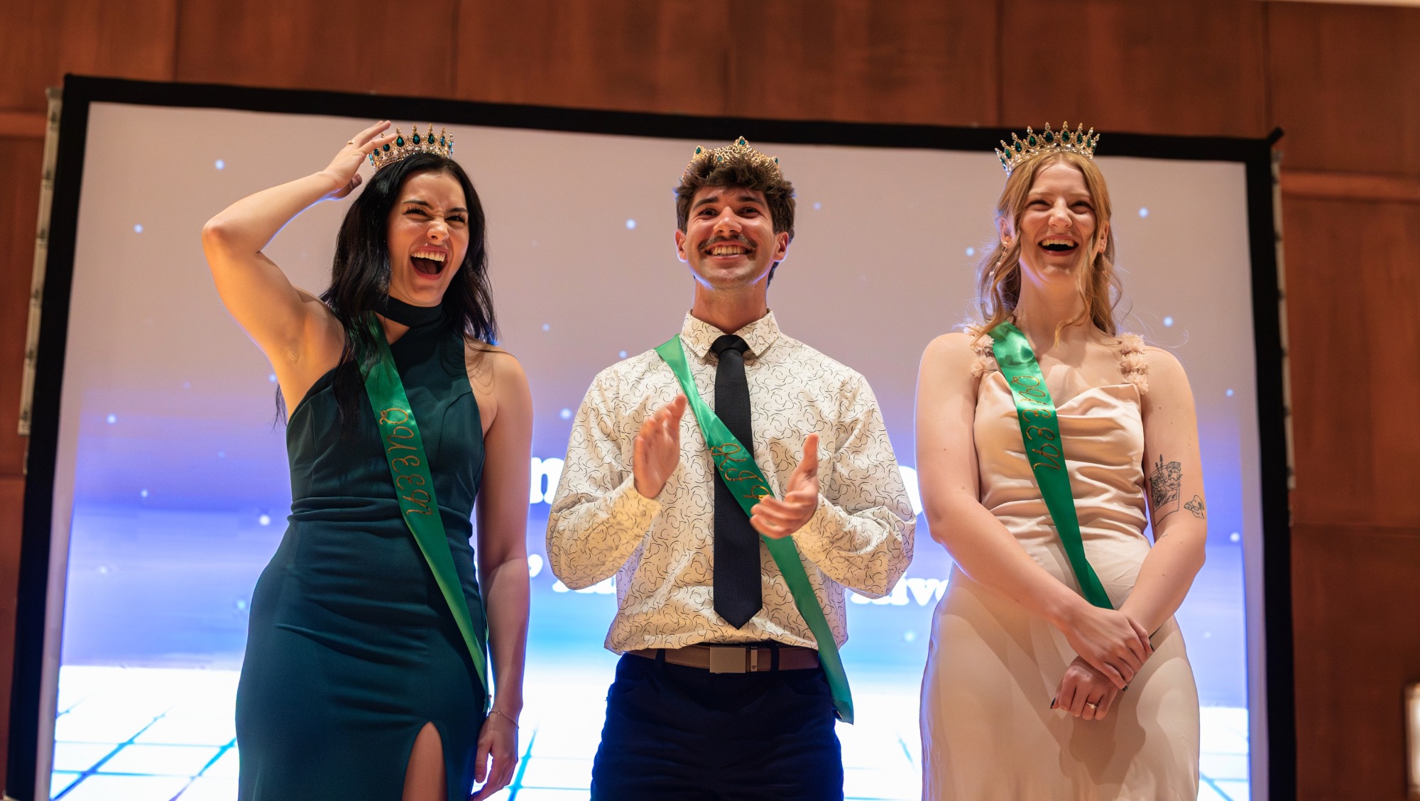 Three people with crowns and sashes smile 
