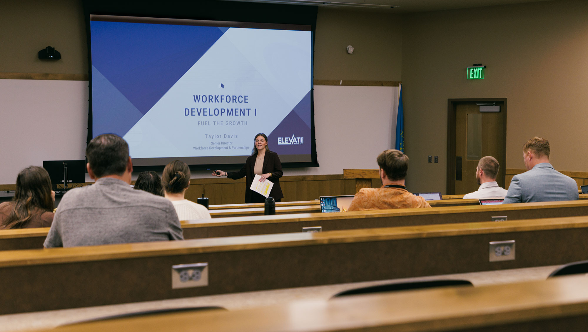 A presenter stands at the front of a classroom at BHSU-Rapid City delivering a presentation on workforce development, while participants sit in tiered seating and follow along on a projected slide during a previous Fuel the Growth event.
