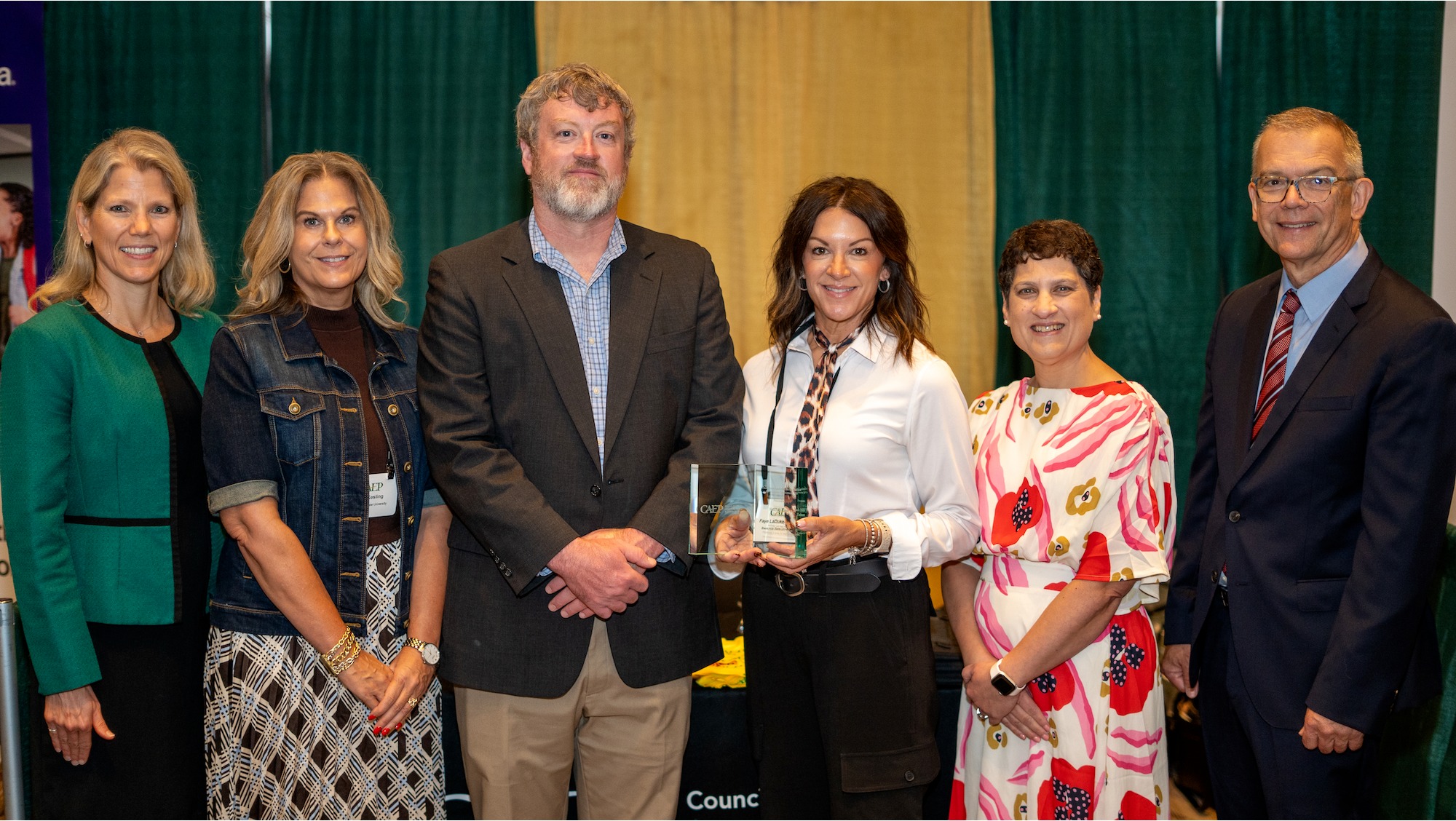 six individuals stand side by side for a group photo while one of them holds onto an award 