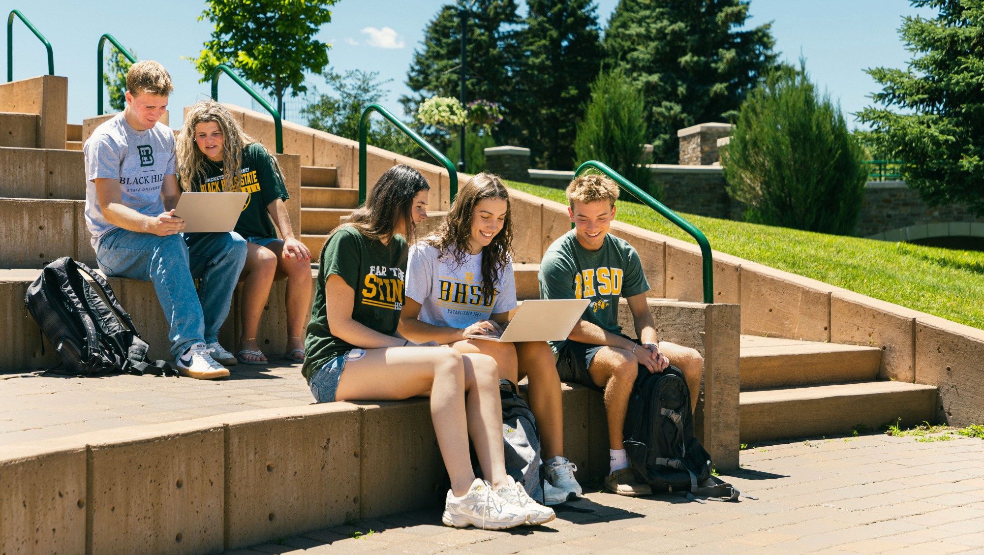 A group of students sit together while looking at their laptops and talking to one another.