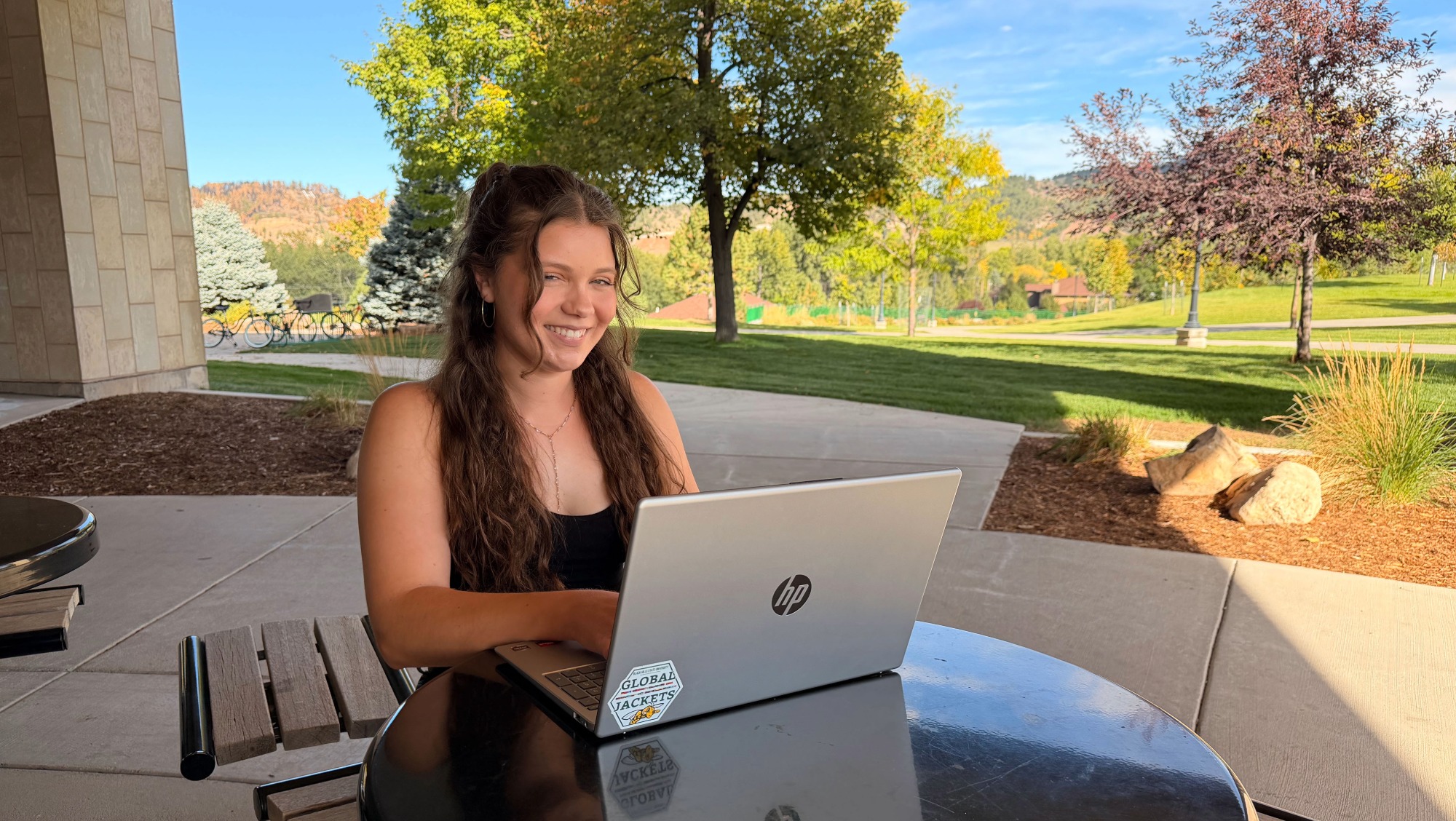 a girl sits at a picnic table outside while working on her laptop.