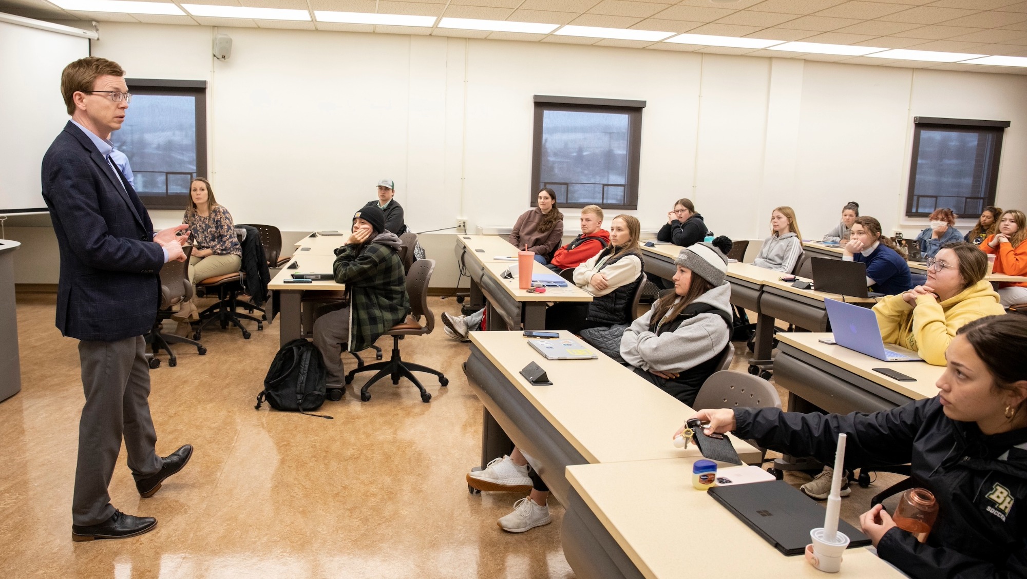 A man stands at the front of a classroom giving a lecture to college students sitting at their desks