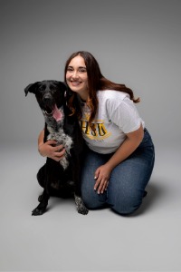 Graduate Torrance Brown kneels next to a dog while smiling for a photo